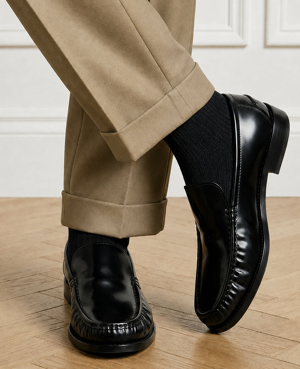 Close detail of Democratique Socks Originals Fine Rib Black worn with black leather penny loafers and tan suede tailored trousers — the definitive black sock and loafer pairing in men's quiet luxury menswear.