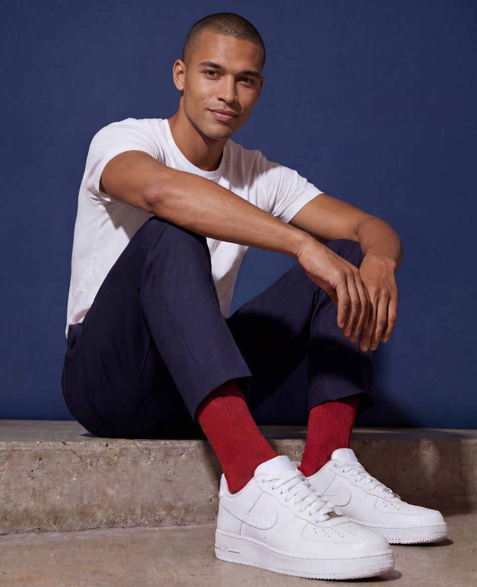 Man wearing Democratique Socks Originals Fine Rib Red Moon with navy trousers, white t-shirt, and white Nike Air Force 1 sneakers — premium organic cotton red socks designed in Copenhagen