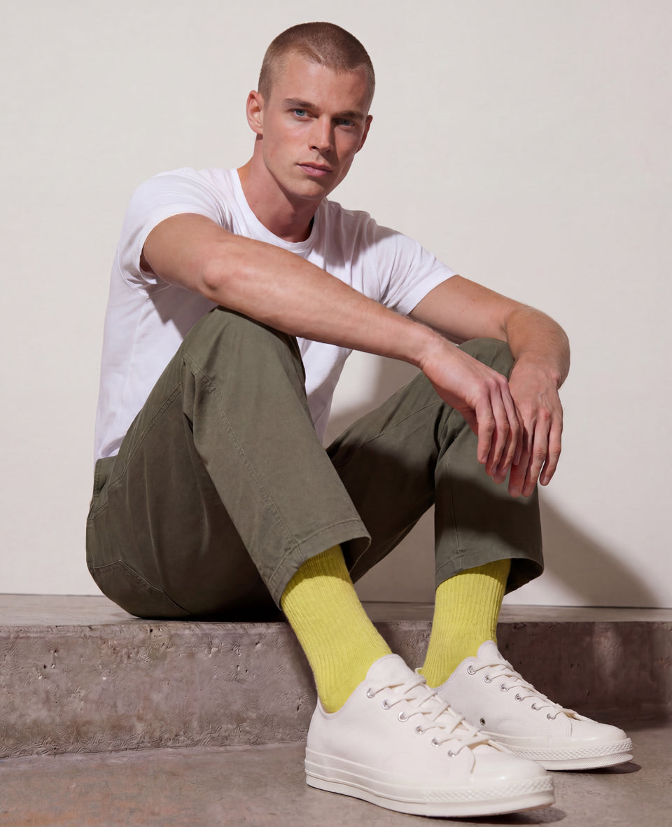 Man in white t-shirt and olive trousers wearing yellow Democratique Yellow Blur ribbed socks and cream Converse sneakers, summer style