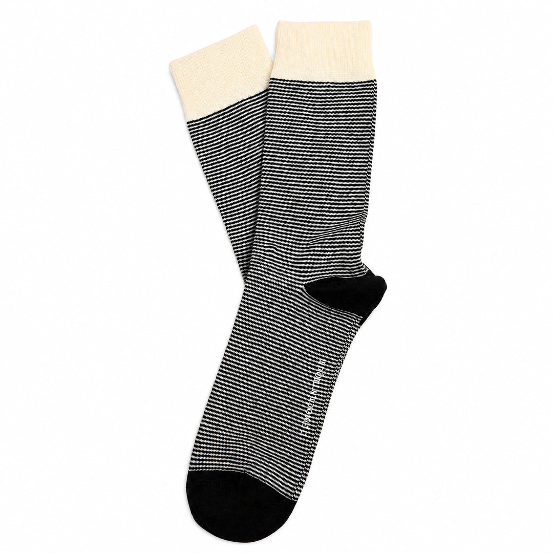 A pair of crew socks with thin black and white horizontal stripes, featuring solid black toes and heels, and a contrasting cream-colored ribbed cuff.